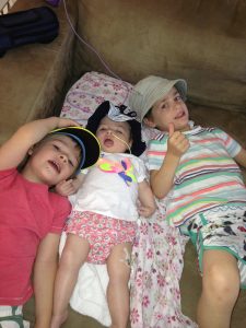 Three children are lying on the a sofa, smiling at the camera.