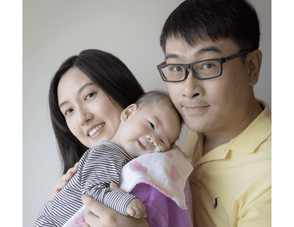 A mum and dad are holding their baby who has a small tube from his nose to help him breathe. They are smiling at the camera.
