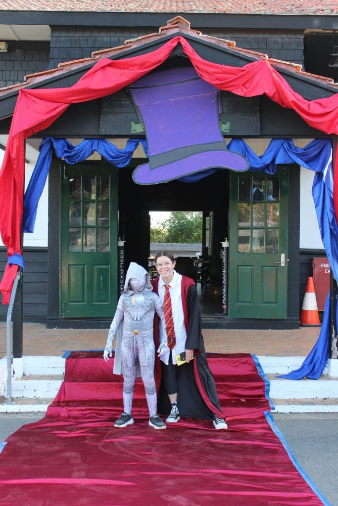 A young woman and a boy pose for a photo on the steps of a building. They are dressed in Harry Potter costumes.