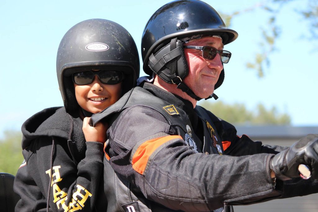 A boy is sitting on the back of a motorbike, with a man riding in front. He is holding on and smiling at the camera.