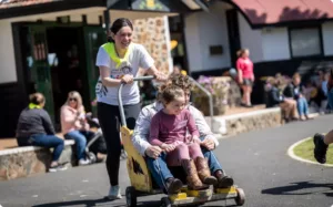 An adult is pushing two people in a cart, they are laughing and smiling