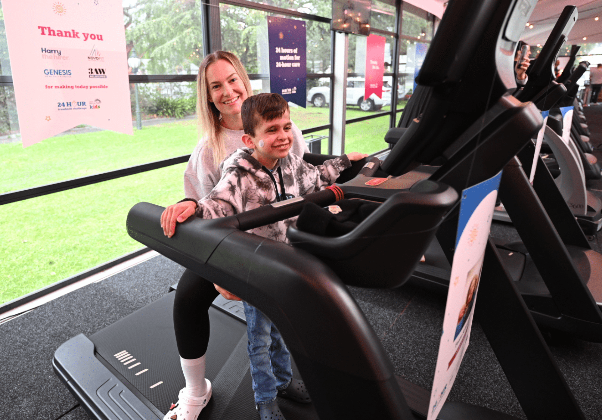 A boy is walking on a treadmill helped by his mum