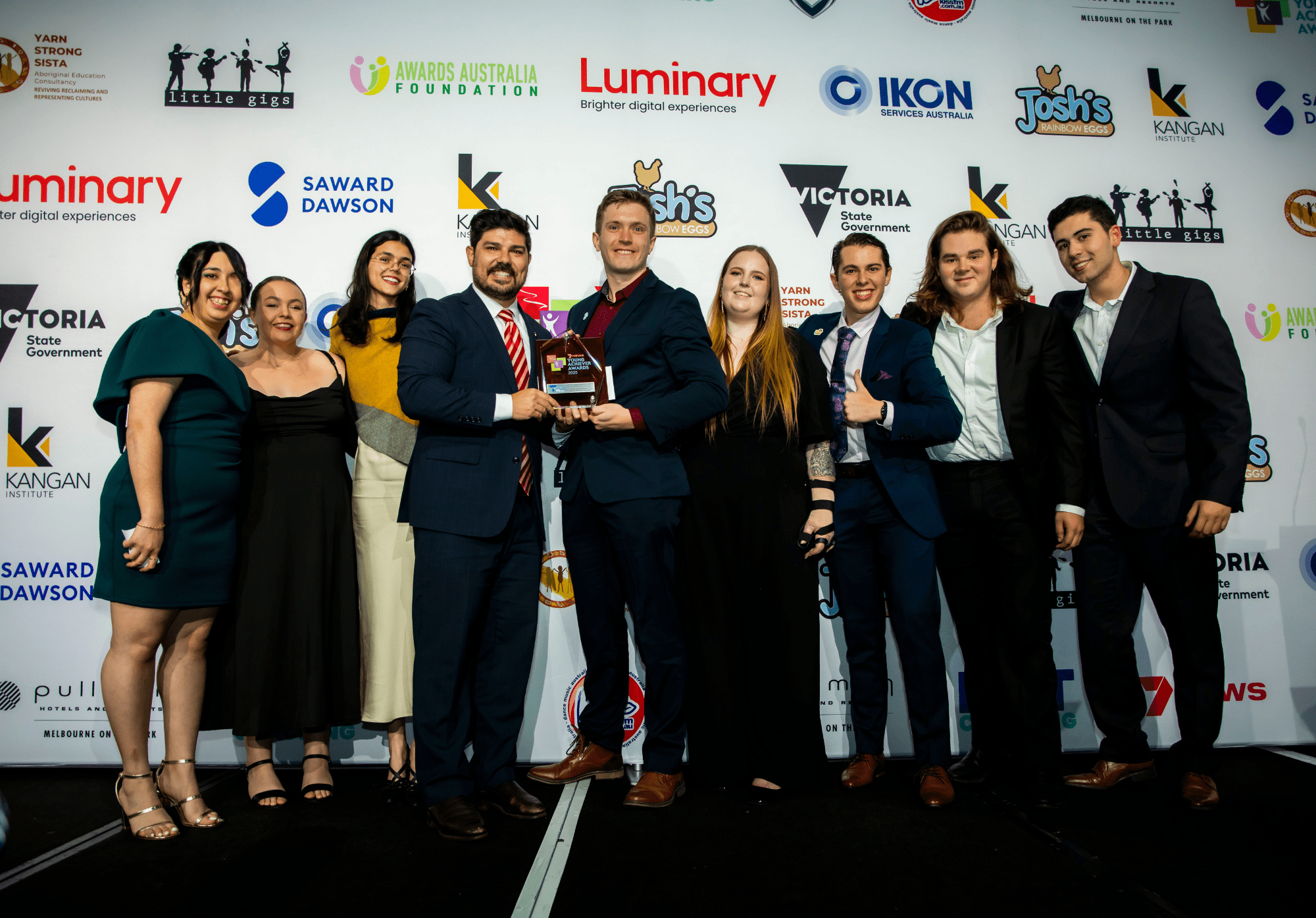 A group of young adults are standing on stage being presented a trophy
