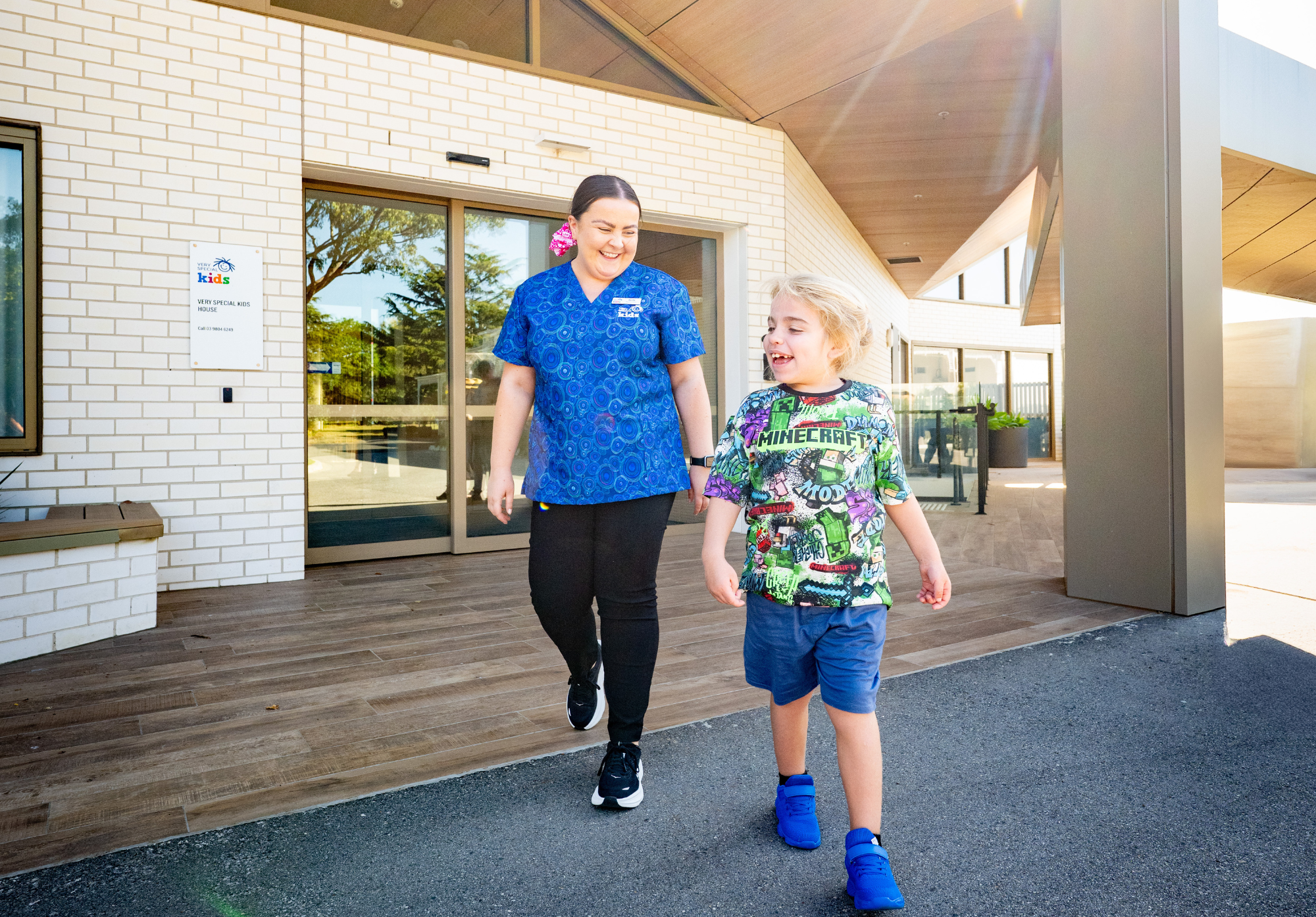 A nurse is smiling at a boy as they walk outside a building.